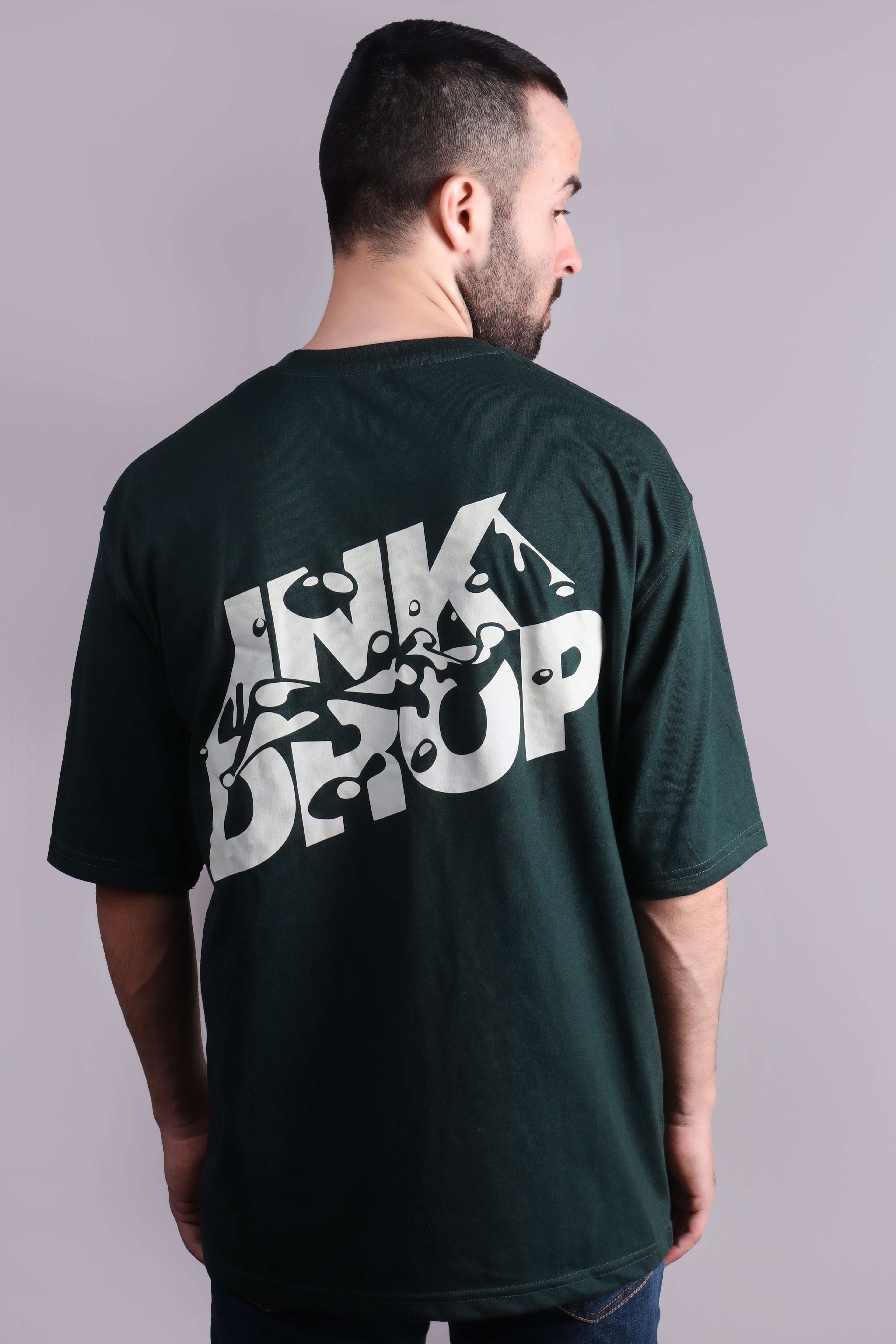 Man wearing a green t-shirt with a white graphic design on the back against a gray background