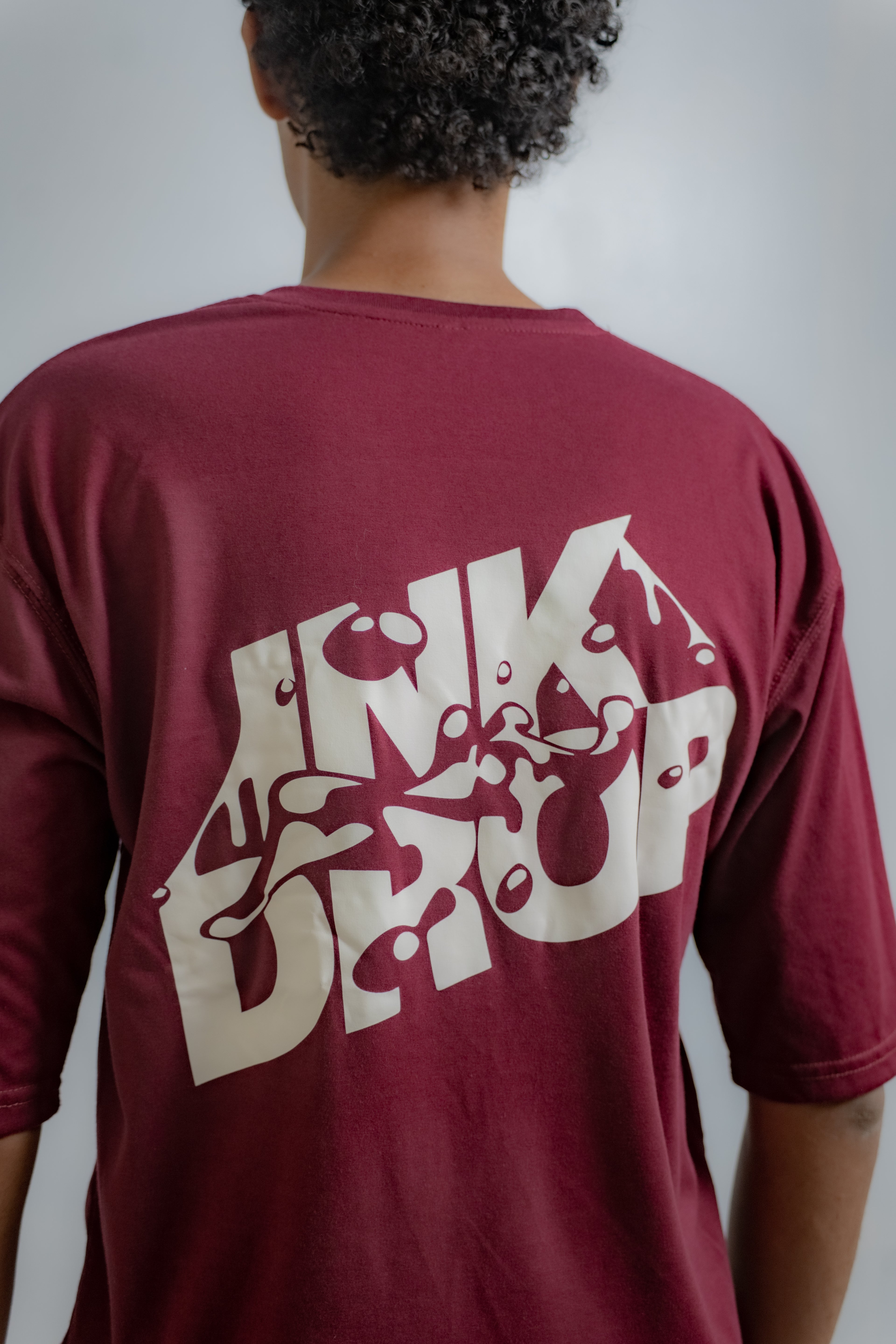 Person wearing a maroon t-shirt with a white graphic design on the back against a plain background