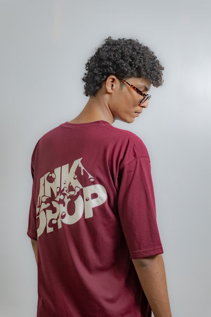Person wearing a maroon t-shirt with 'INK DROP' printed on the back against a plain background