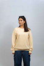 Woman wearing a beige sweater and blue jeans against a plain background