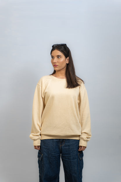 Woman wearing a beige sweater and blue jeans against a plain background