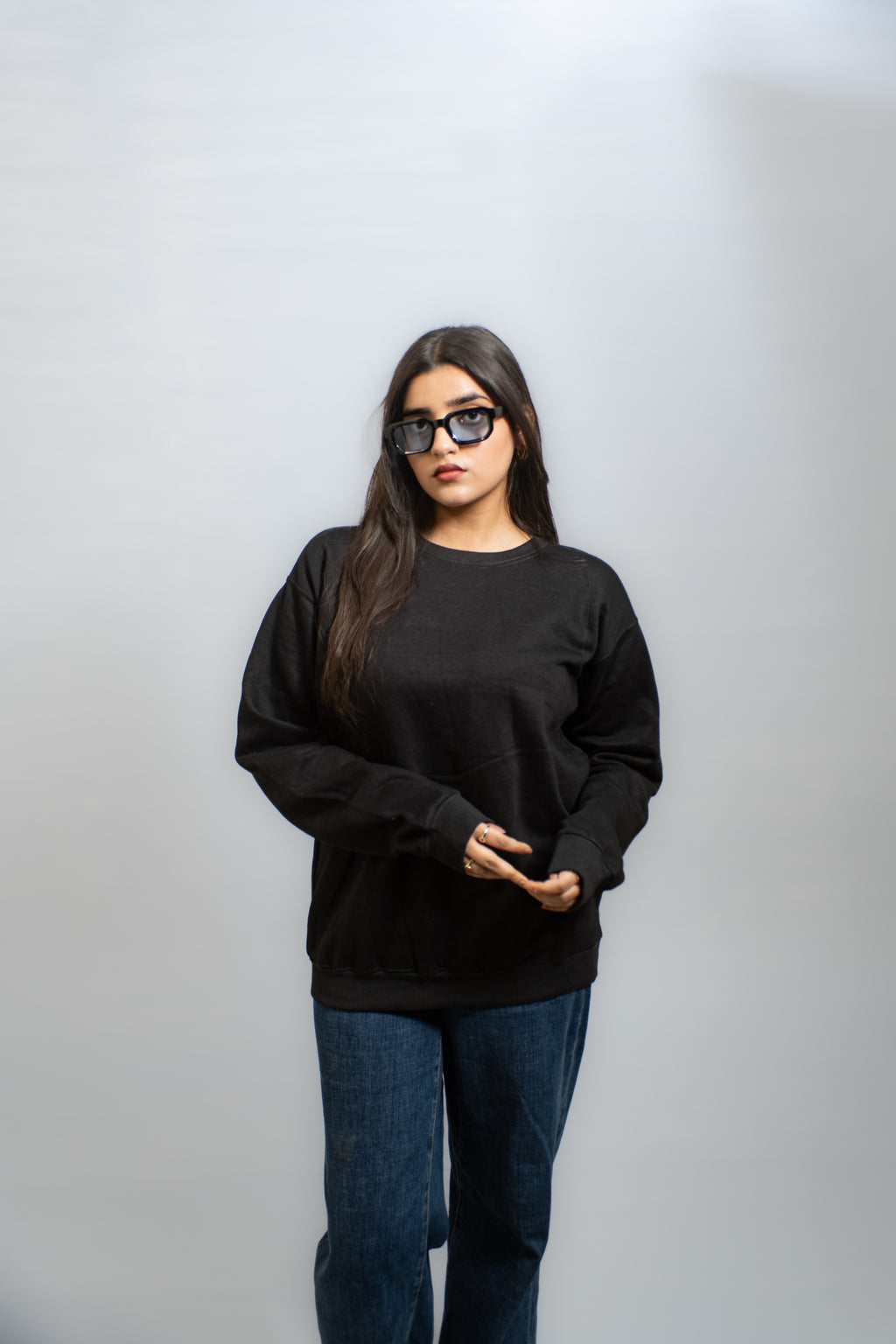 Person wearing a black sweatshirt and blue jeans against a plain background