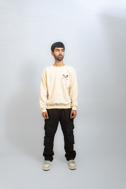 Man wearing a beige sweatshirt and black pants on a plain background