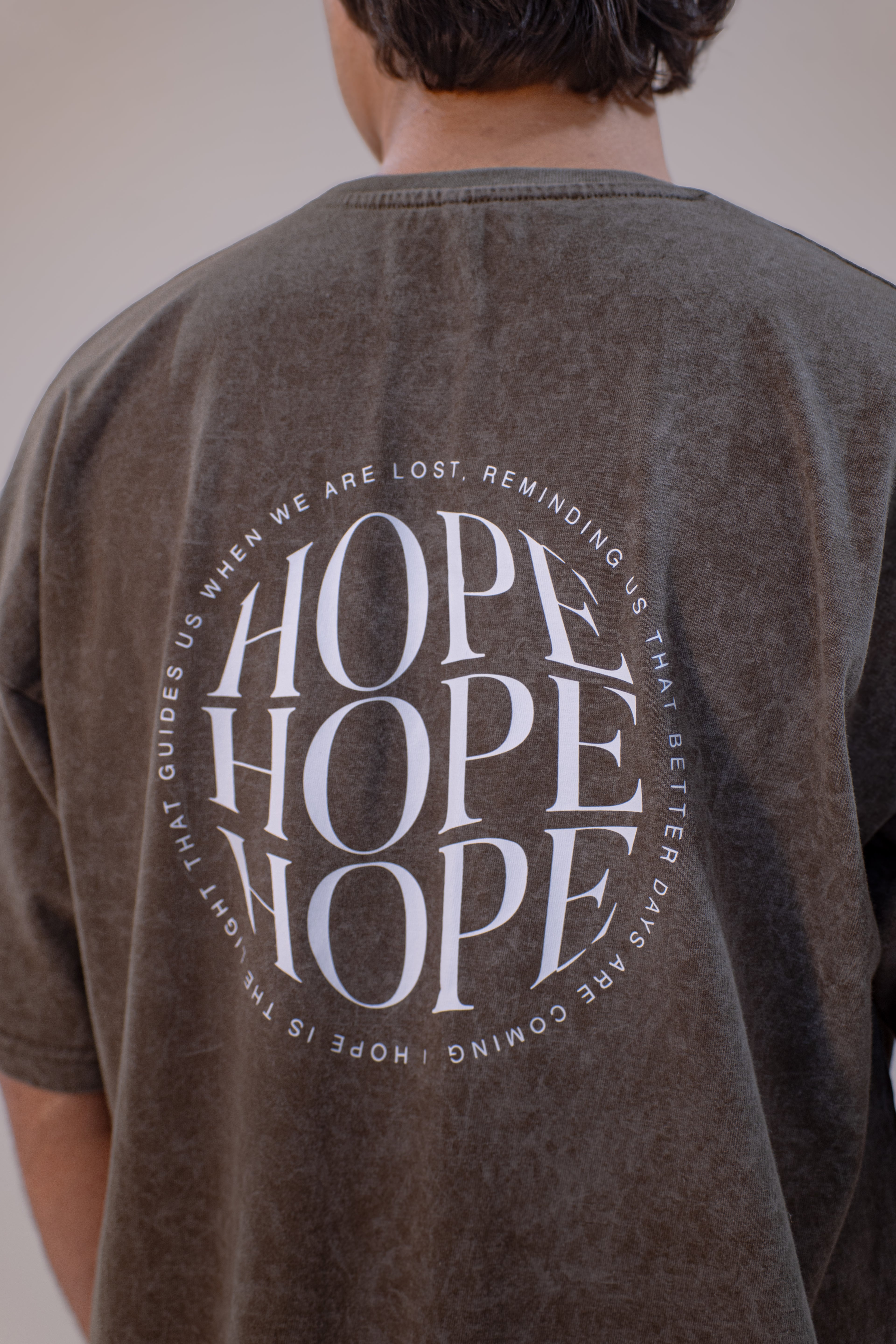 Person wearing an olive acid wash t-shirt with 'HOPE' text on the back.